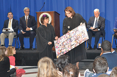 Chief Justice Rush holds a large board covered with photos of children who she hosted in her courtroom during her time as a trial court judge.