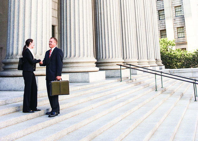 Full length side view of male and female attorneys shaking hands on courthouse steps