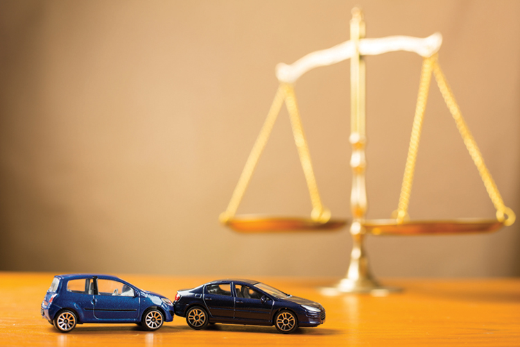 Toy cars involved in a collision are featured in the foreground of an image with gold scales of justice in the background.