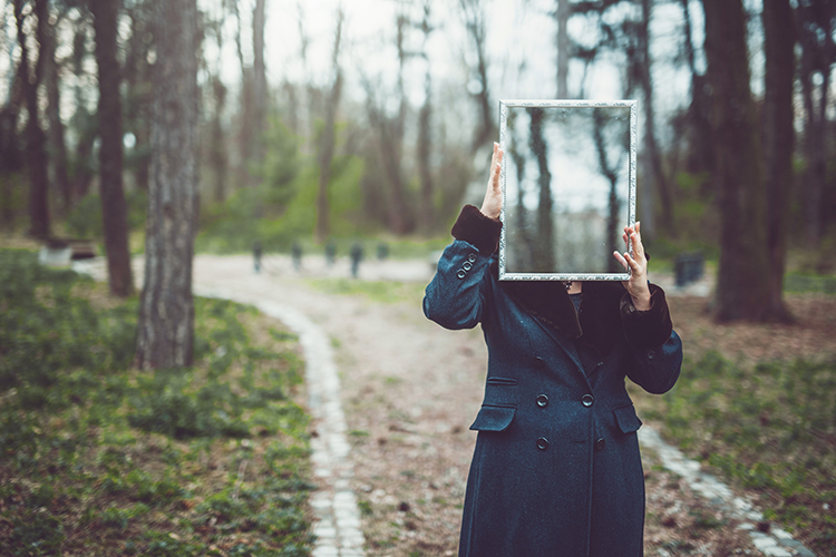 Woman stands holding a mirror where her face should be
