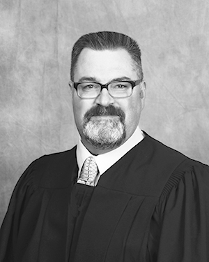 Black and white head shot of Magistrate Michael Cox, wearing black judges' robes.