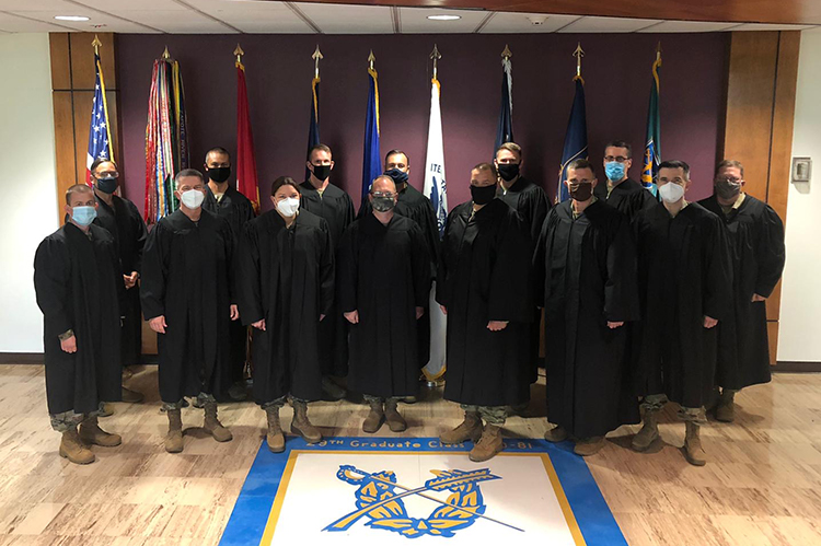 Group of army students wearing black judges' robes, standing in front of flags.
