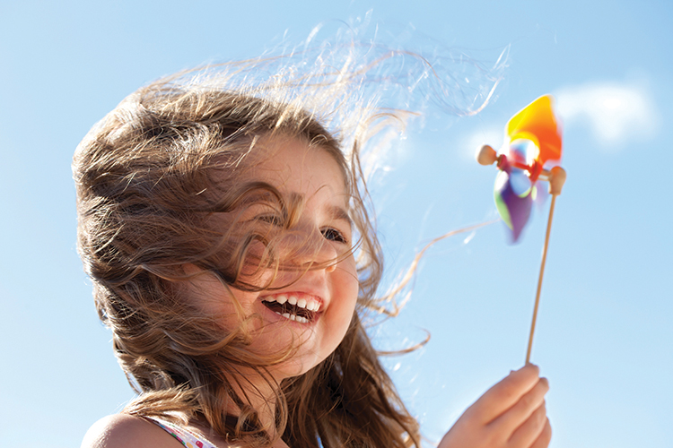 Little happy girl laughing and holding a pinwheel in front of a bright sky. The wind is blowing her hair illuminated by the sunlight. Conceptual image about environment and happiness.Similar pictures: