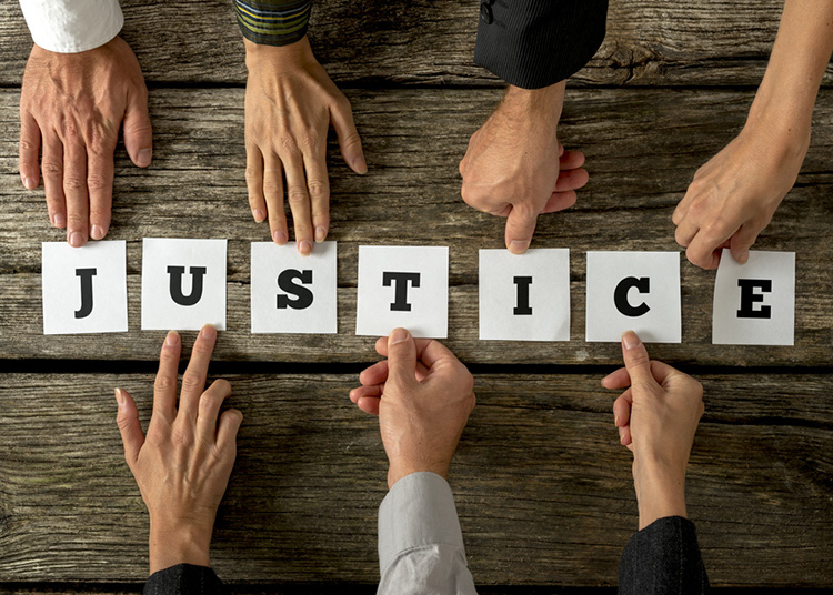 Seven people assembling the word Justice with white cards and letters on them over rustic textured wooden desk.