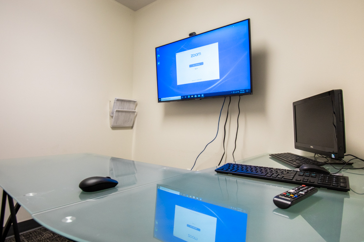 A TV displaying videoconferencing software is mounted in a wall above a desk.