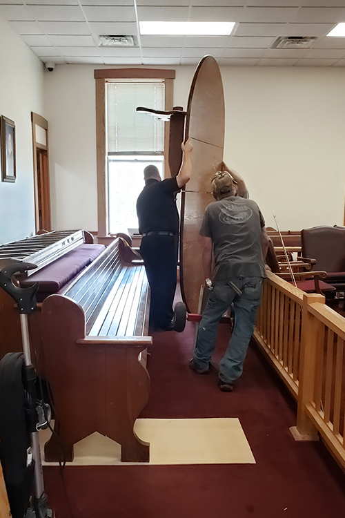 Men walk a table standing up on its end down a narrow passage in the courtroom.