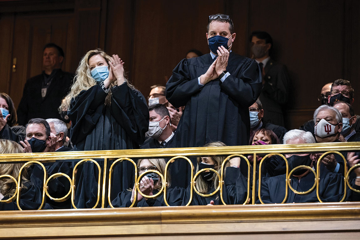 Judges in black robes stand and applaud.