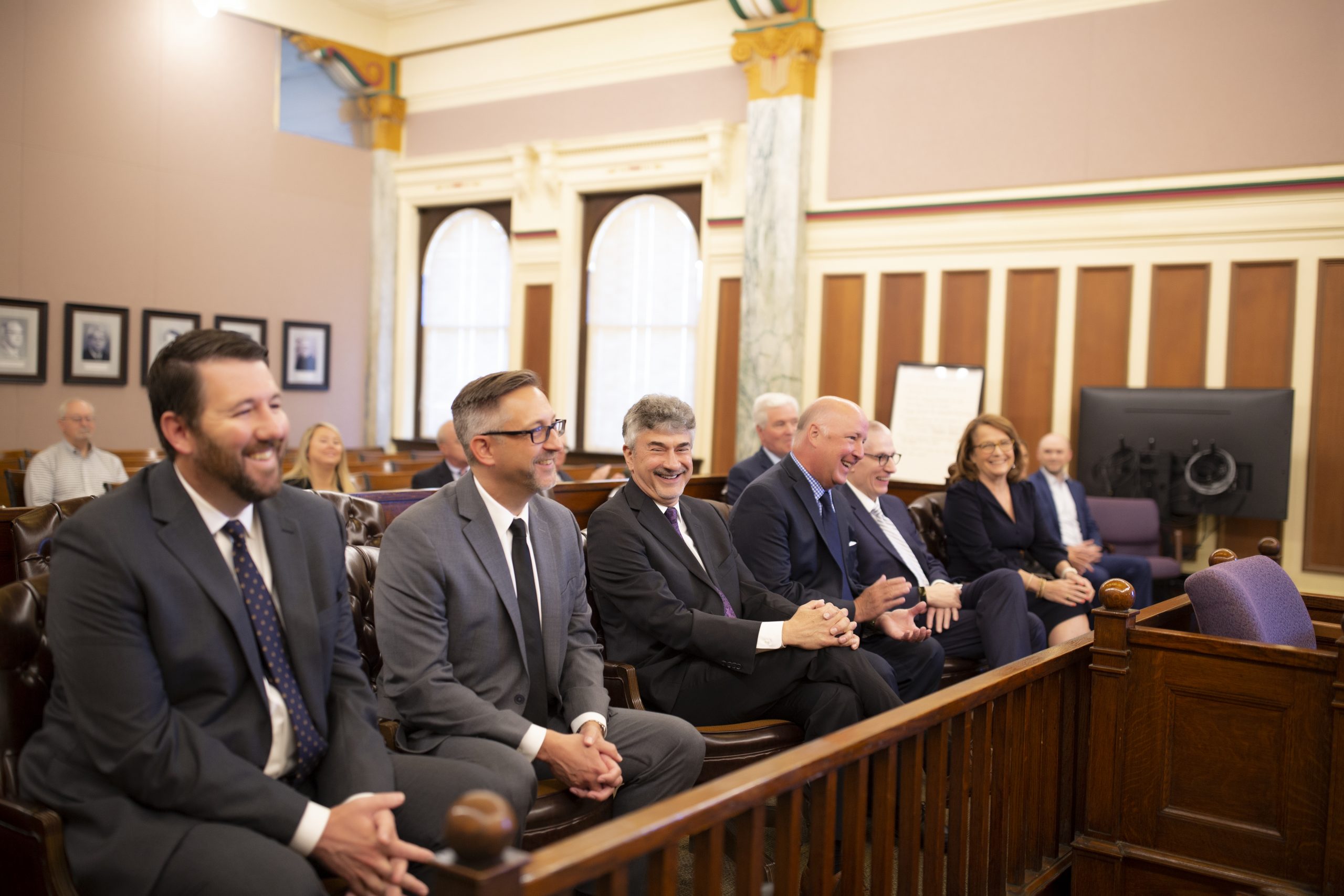 Justices sitting in the front row of the courtroom smiling.