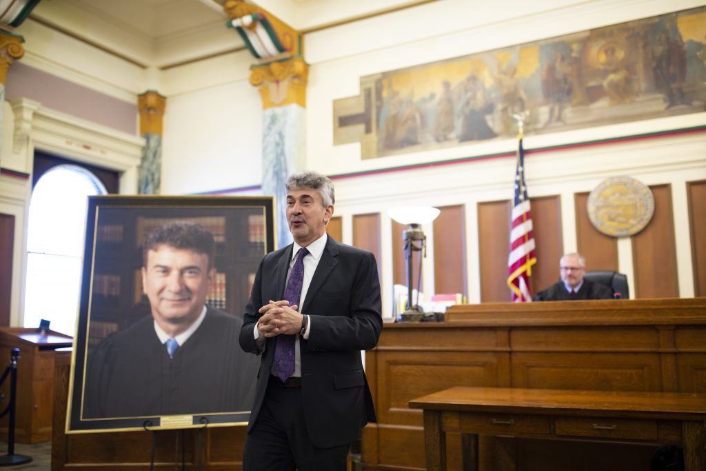 Justice David stands beside his portrait and addresses those gathered