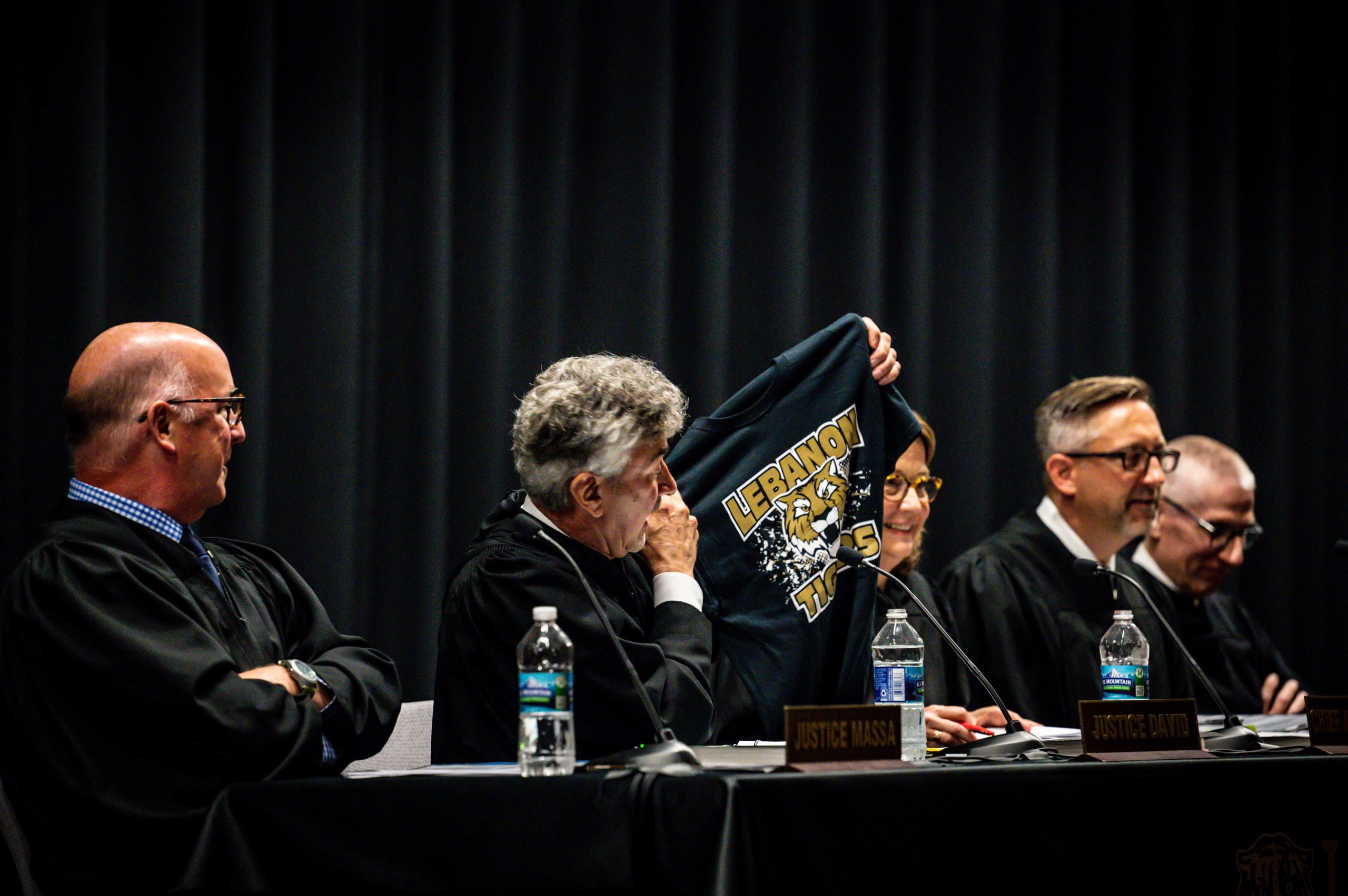 The five Justices sitting at the traveling bench at Lebanon High School with Justice David holding up a Lebanon Tigers t-shirt.