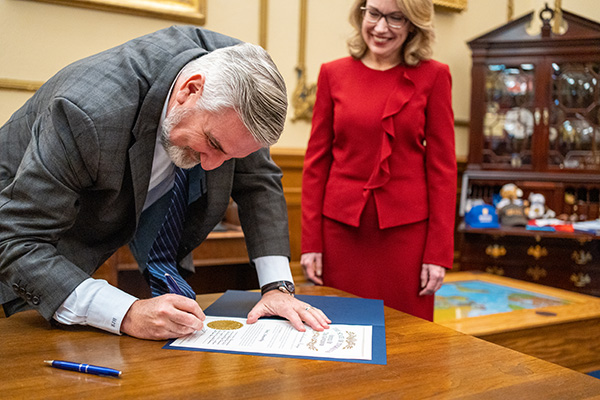 Governor Eric Holcomb signs a declaration with Judge Dana Kenworthy standing behind him.