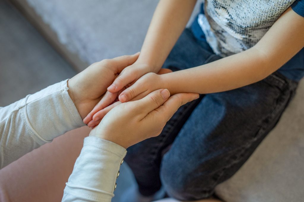 An adult holds a child's hands in theirs.