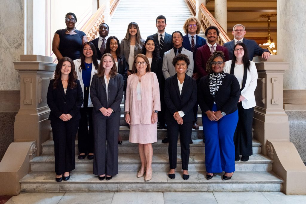 Chief Justice Loretta Rush stands on the stairs at the Indiana Statehouse aside the 16 2024 ICLEO fellows.