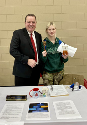 Judge Jeffirs and a high school student pose for a photo in front of a table with materials for students to take at a career fair.