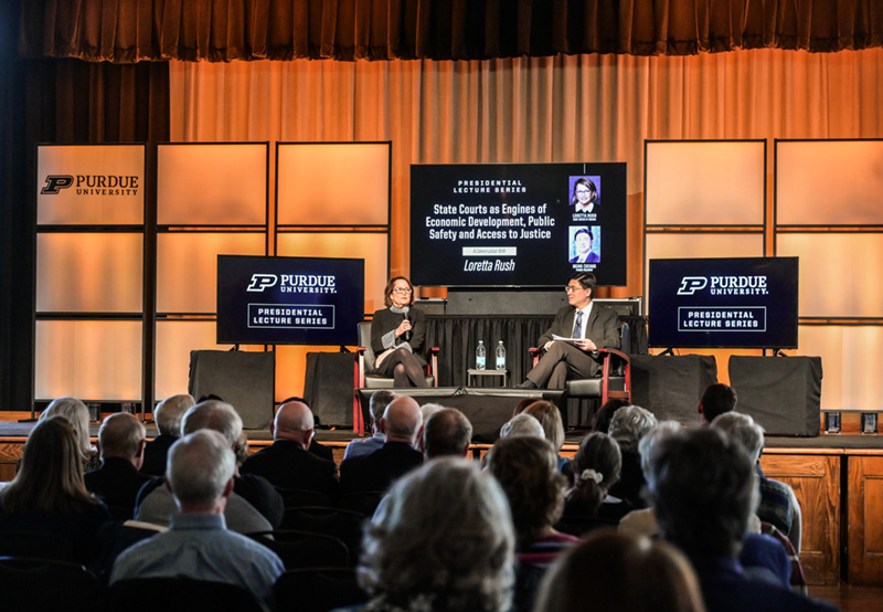 Chief Justice Loretta Rush and Purdue President Mung Chiang on the stage in front of an audience at a university auditorium.
