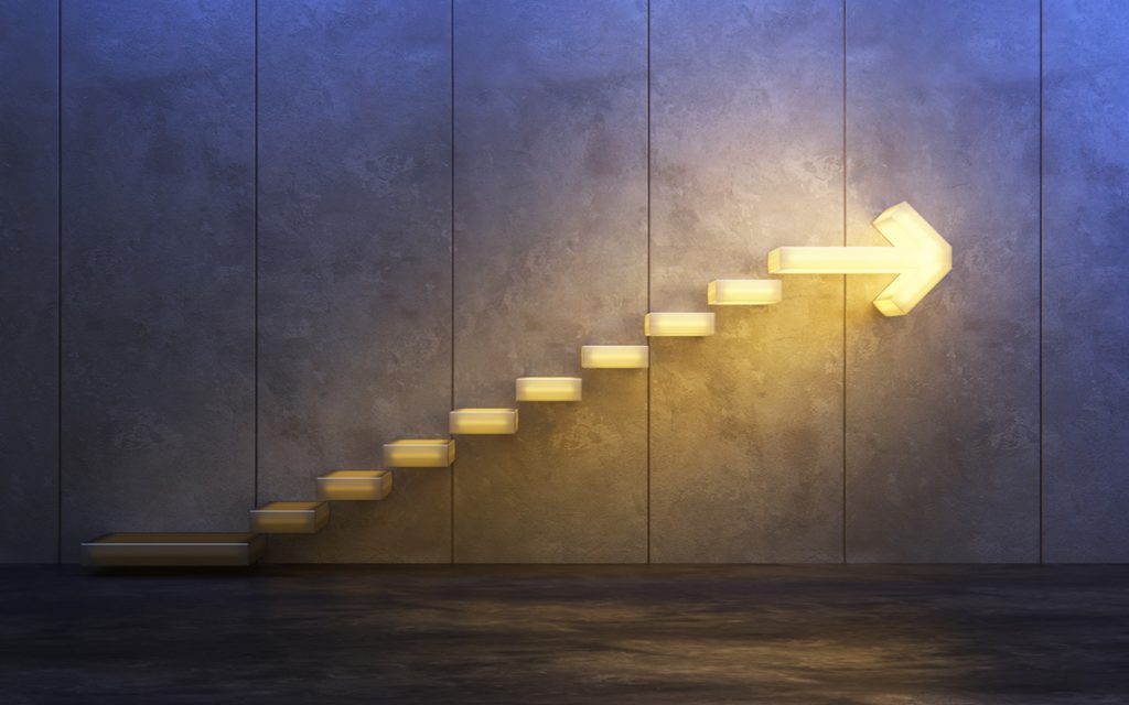 Lighted steps on a wall getting brighter as they lead toward an arrow pointing to the future.