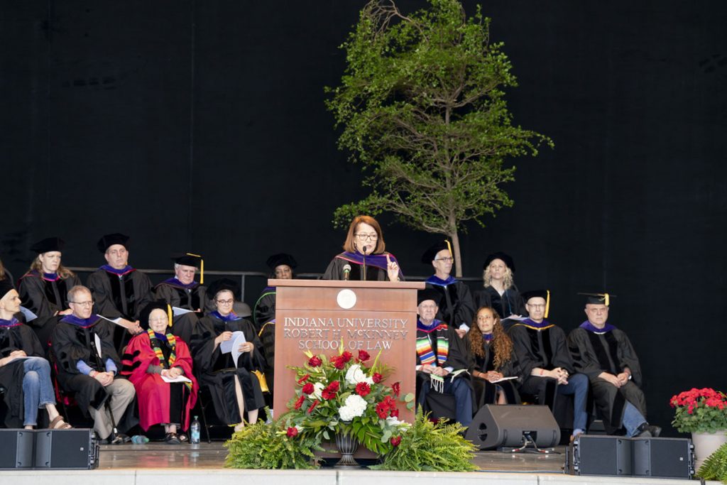 Chief Justice Rush stands at a podium with other distinguished people seated behind her. 
