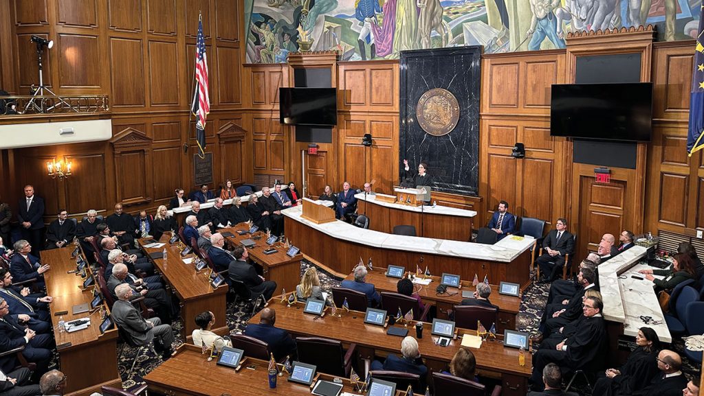 Chief Justice Loretta Rush at the podium in the House Chamber raising a hand to honor a special guest during the 2026 State of the Judiciary.