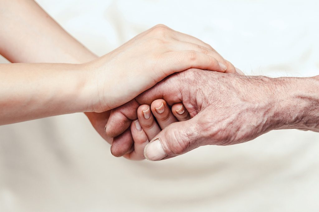 The hand of an elderly person is held by the hands of someone younger.