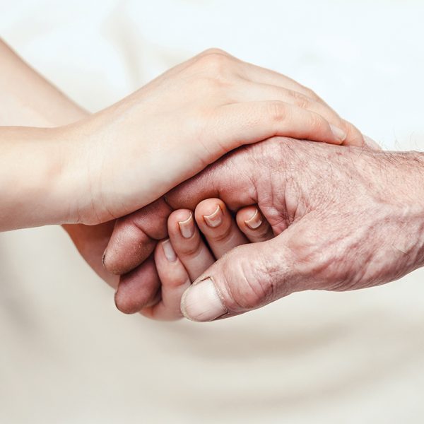The hand of an elderly person is held by the hands of someone younger.