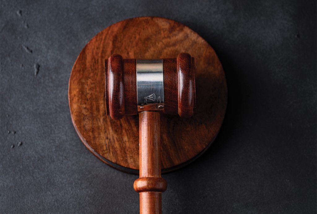 A wooden judge's gavel resting on a matching round sound block against a dark textured background.