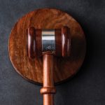 A wooden judge's gavel resting on a matching round sound block against a dark textured background.