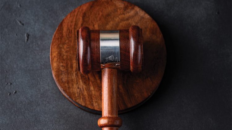 A wooden judge's gavel resting on a matching round sound block against a dark textured background.